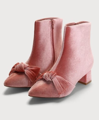 A pair of pink vegan velvet boots featuring a bow