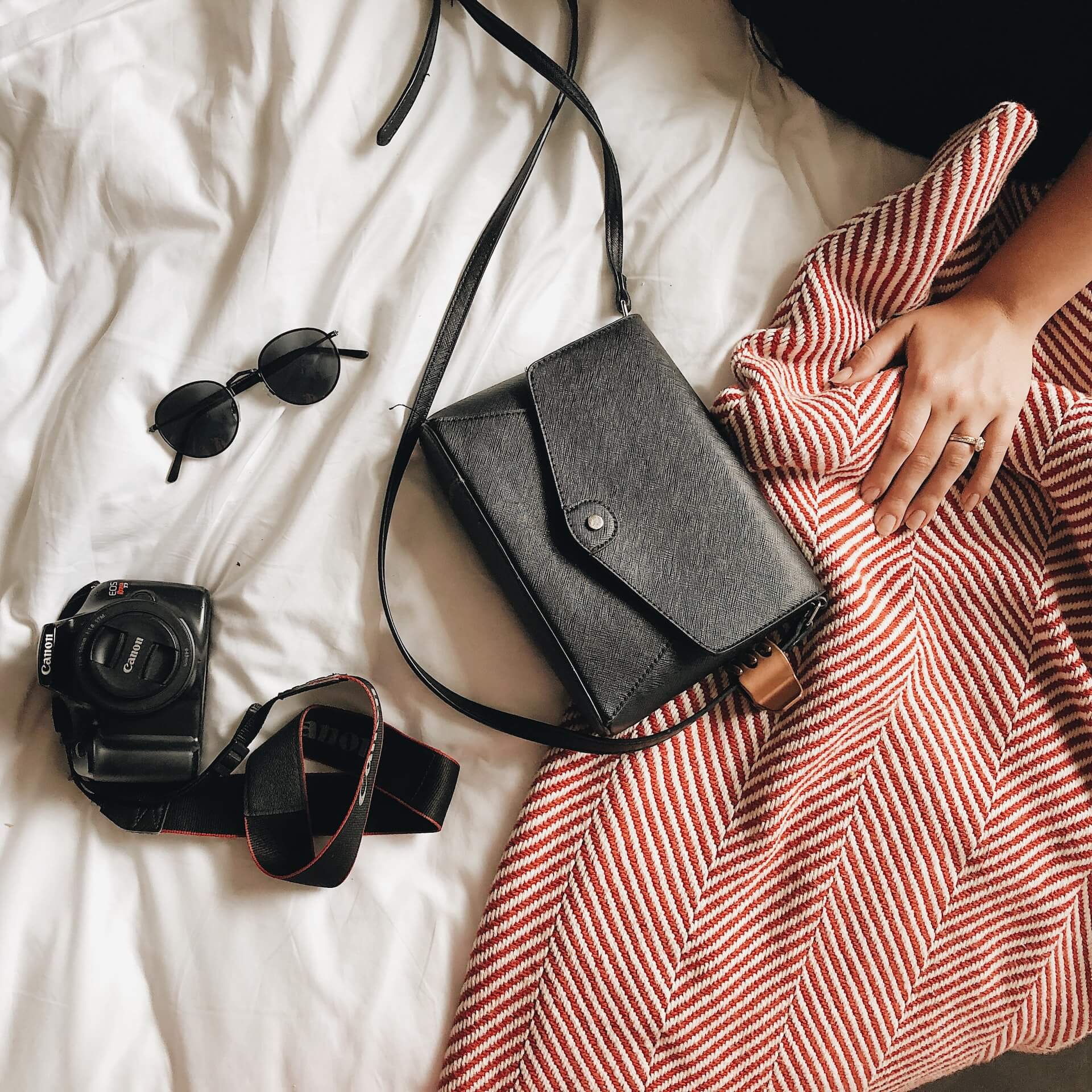 Black sunglasses, a black purse, and a DSLR camera lie on a bed comforter