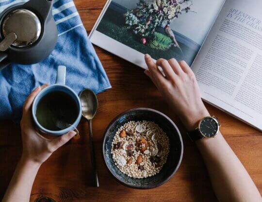 Person reading while eating a healthy vegan oatmeal bowl and a cup of tea.
